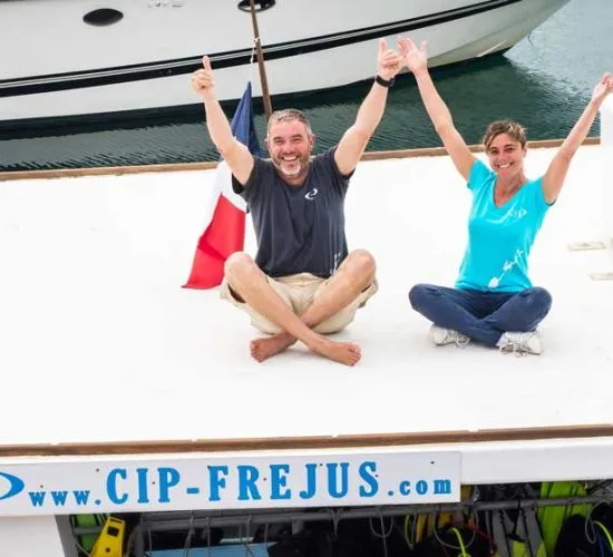 Deux personnes souriantes lèvent les bras sur un bateau en mer