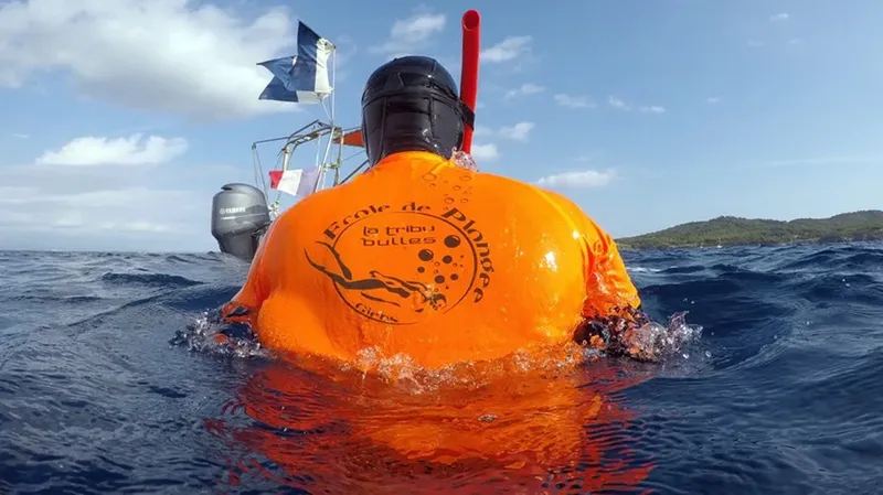 Plongeur en surface avec gilet de signalisation orange et bateau en arrière