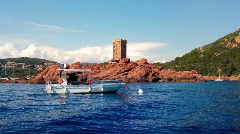 Bateau de plongée en mer devant une côte rocheuse et une tour