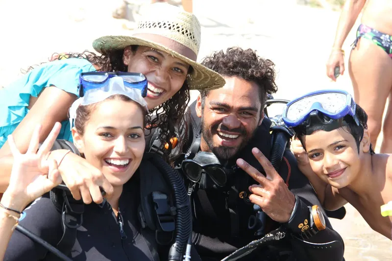 Groupe de plongeurs souriants avec leur équipement sur la plage
