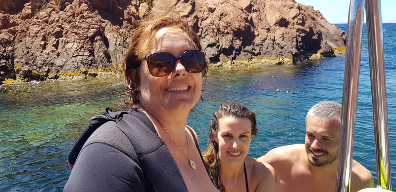 Trois personnes souriantes sur un bateau en mer, côte rocheuse