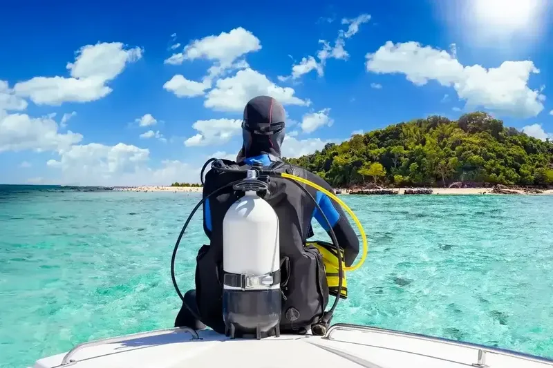 Plongeur équipé sur un bateau, vue sur une île tropicale