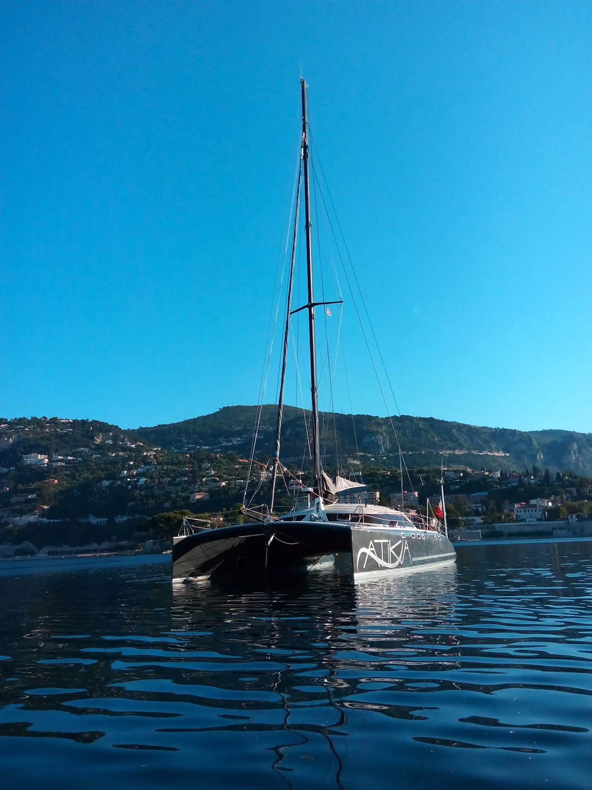 Catamaran noir amarré sur l'eau calme avec des collines en arrière-plan