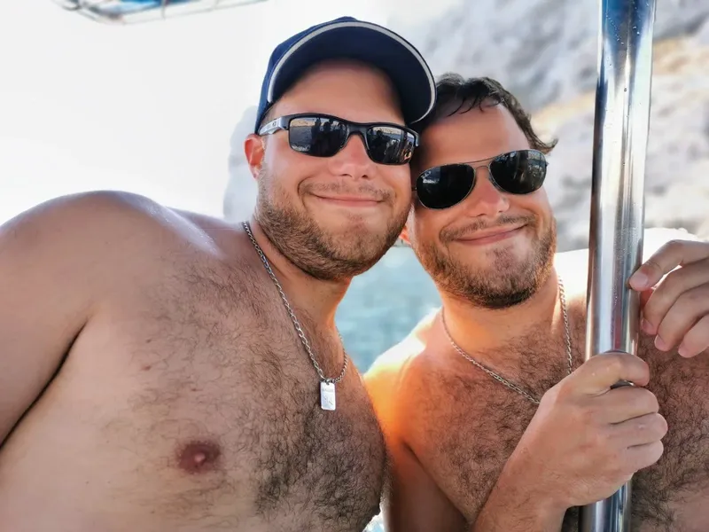 Deux hommes souriants, torse nu et lunettes de soleil, sur un bateau
