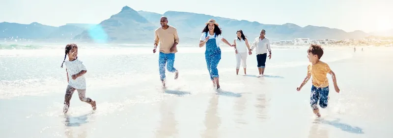 Famille courant sur une plage de sable, vagues et montagnes en arrière-plan