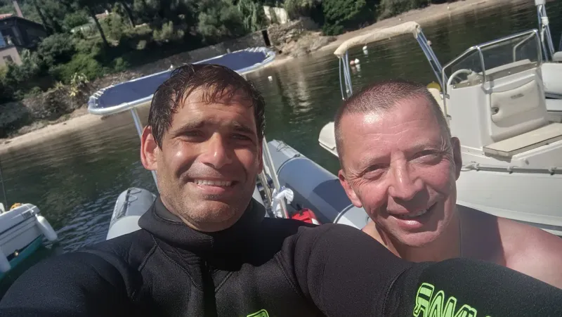 Deux hommes souriants, en combinaison, près de bateaux à quai