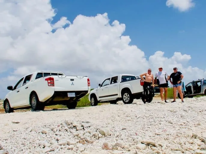 Trois personnes se promènent près de pick-ups blancs sur un sol rocailleux