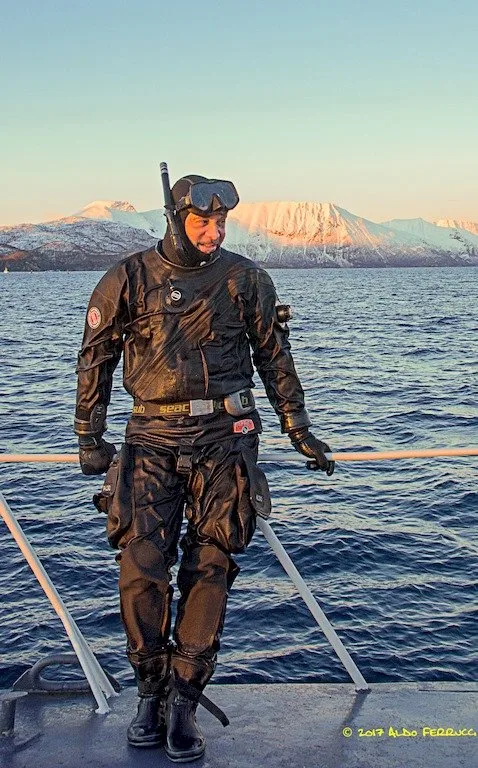 Plongeur en combinaison complète sur un bateau, mer et montagnes