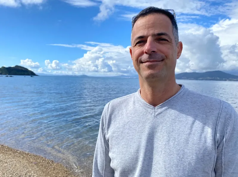 Homme souriant sur une plage ensoleillée avec la mer en arrière-plan