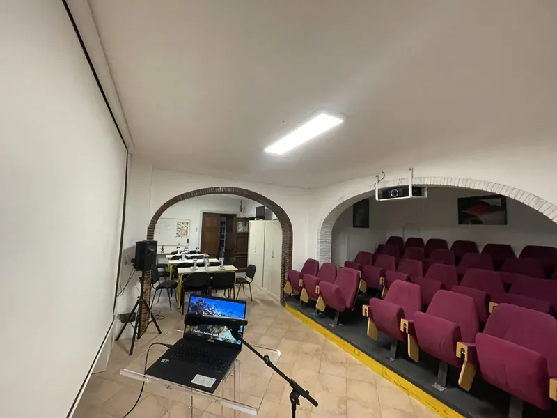 Salle de cours avec des sièges rouges, un ordinateur et un projecteur