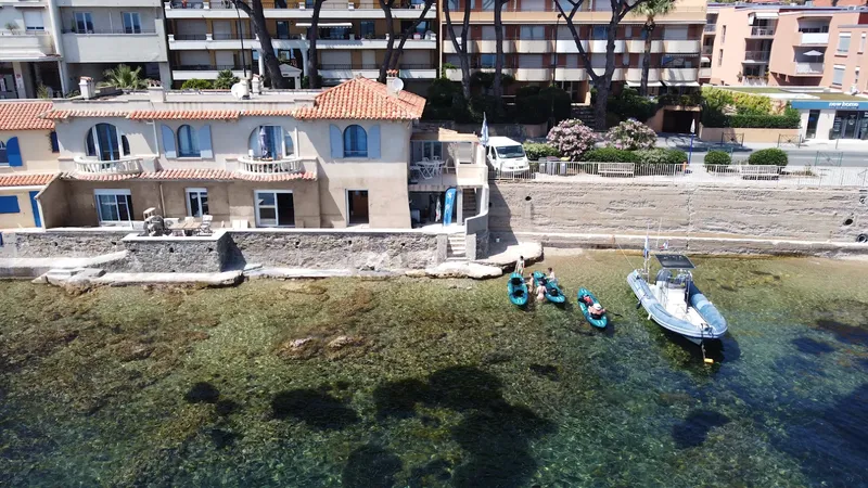 Bâtiment face à la mer, kayaks et bateau amarrés, personnes présentes