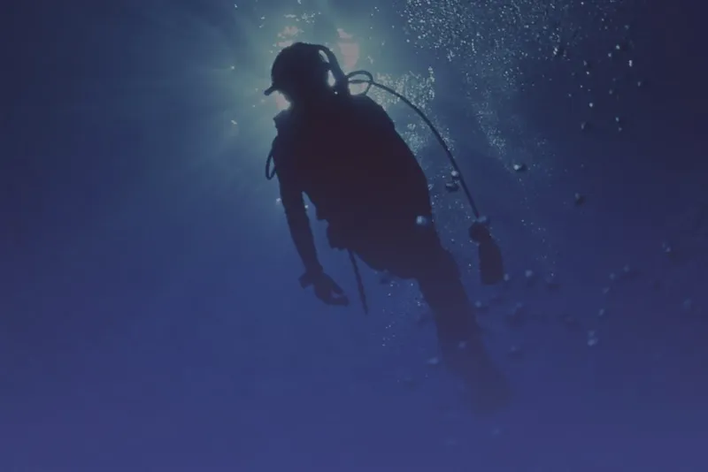 Plongeur silhouetté nageant vers la surface dans l'eau bleue