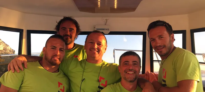 Cinq hommes souriants sur un bateau, en t-shirts verts, regardant la caméra