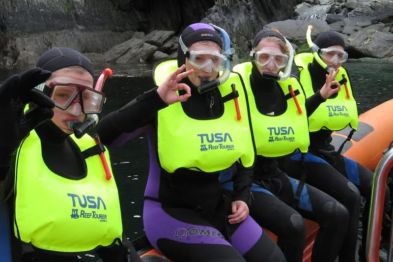 Quatre plongeurs souriants avec gilets et masques sur un bateau