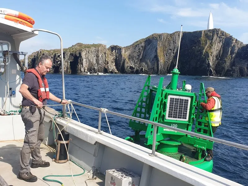 Deux hommes sur un bateau, devant une côte rocheuse et verte