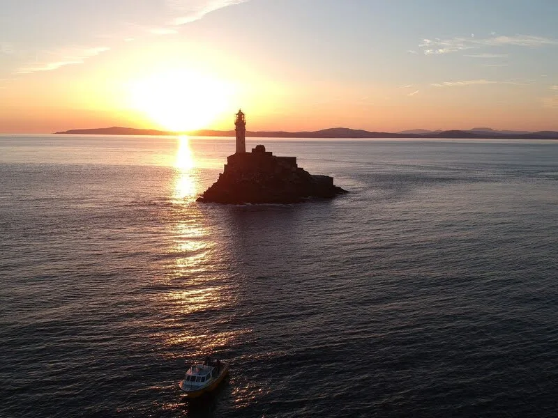 Phare sur un rocher en mer au coucher du soleil avec bateau