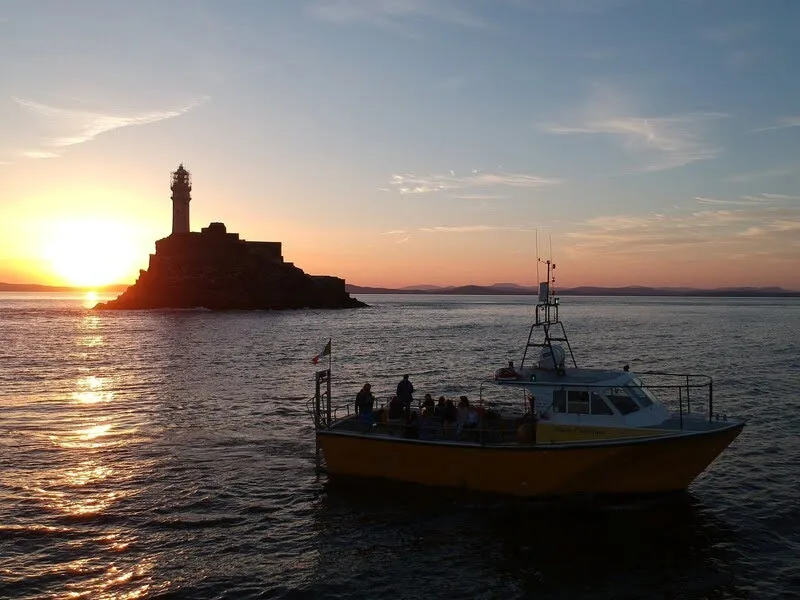 Bateau de passagers jaune naviguant face à un phare au coucher du soleil
