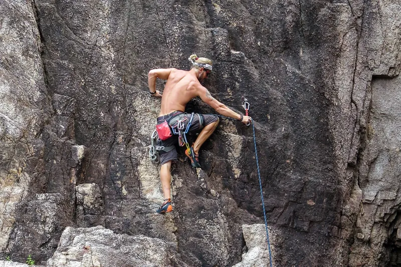 Un homme escalade une paroi rocheuse verticale avec du matériel