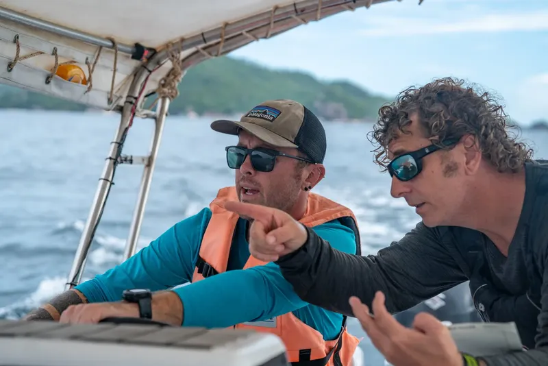 Deux hommes pointent vers l'horizon en mer, portant des lunettes