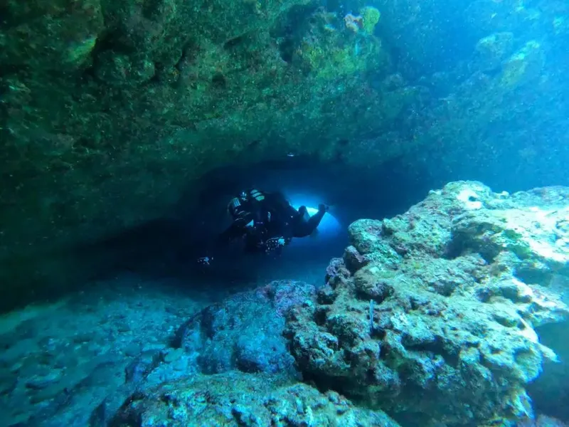 Plongeur explorant une grotte sous-marine rocheuse avec une lumière vive