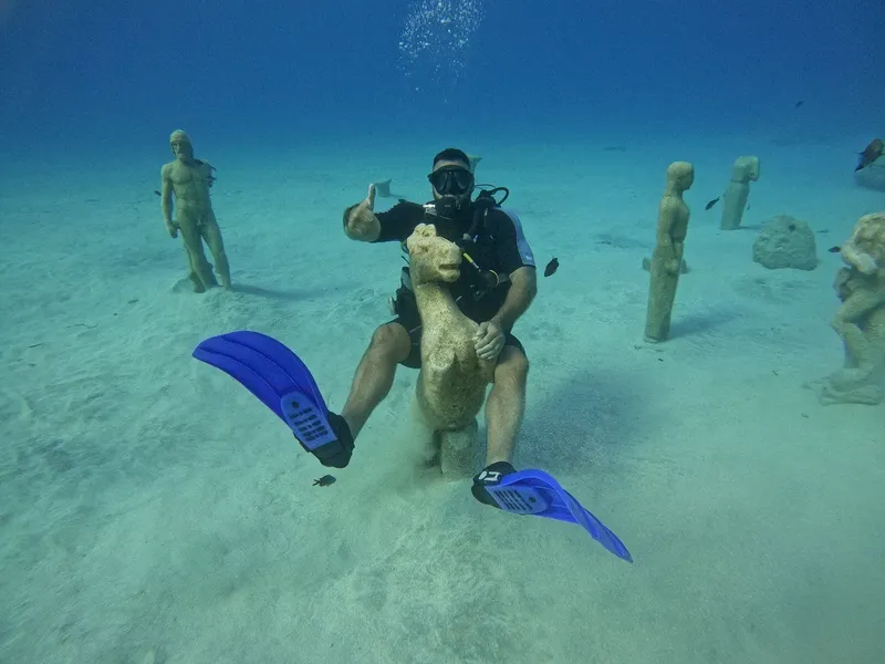 Plongeur souriant sur une statue sous-marine dans un fond sableux