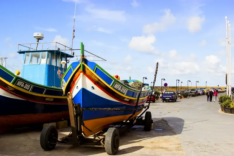Bateaux de pêche colorés sur remorque, parking et personnes au loin
