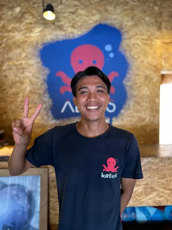 Homme souriant faisant un signe de la main devant un mur décoré
