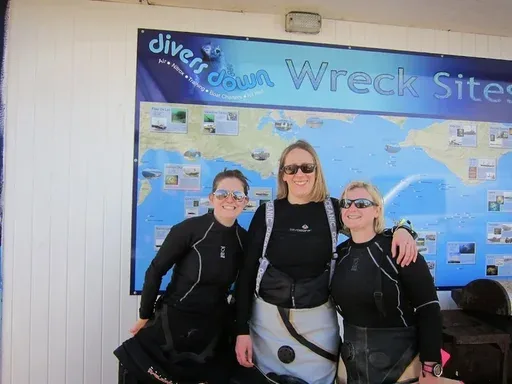 Trois plongeuses souriantes posent devant une grande affiche de sites