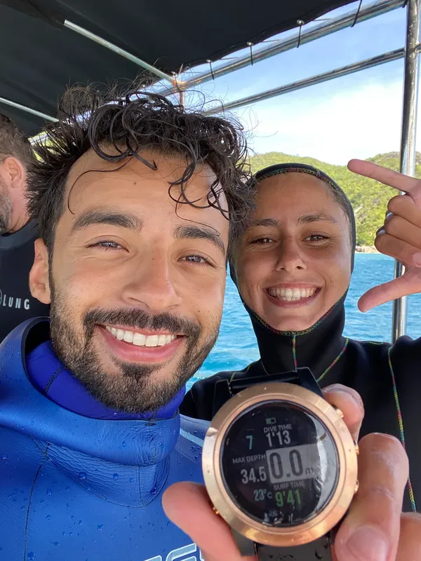 Deux plongeurs souriants sur un bateau, avec un ordinateur de plongée