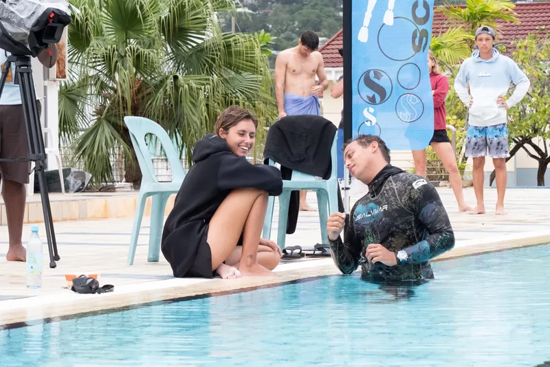 Deux personnes discutent au bord d'une piscine, d'autres personnes attendent