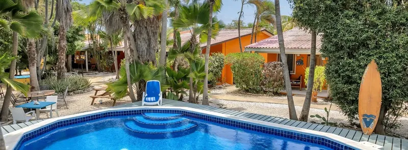 Piscine bleue devant bâtiments colorés et végétation tropicale luxuriante