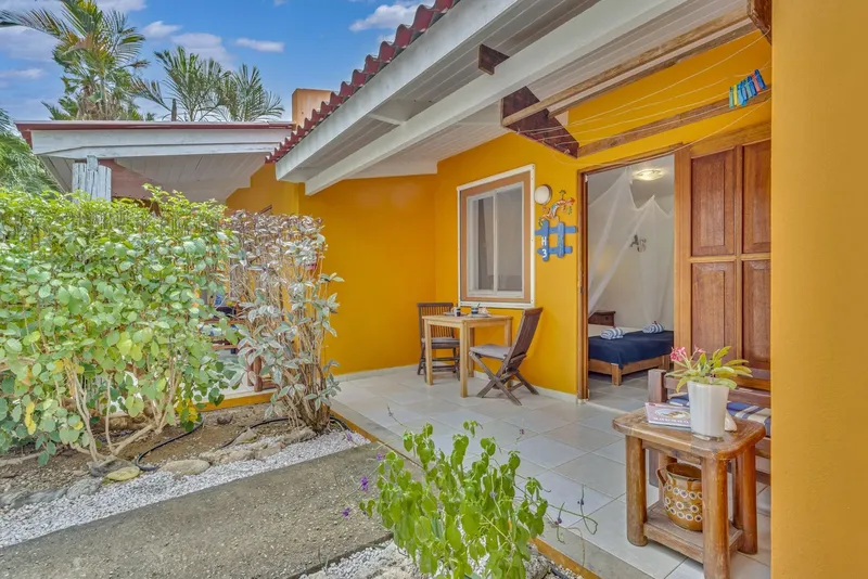 Terrasse devant un bungalow jaune avec table, chaise et plante