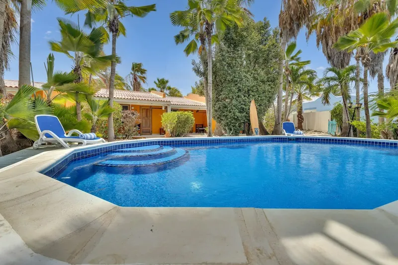 Piscine extérieure avec transats, bâtiments et palmiers sous ciel bleu