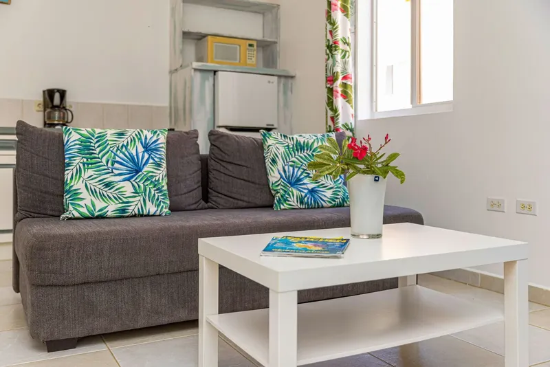 Canapé gris avec coussins tropicaux, table basse et fleurs dans un intérieur