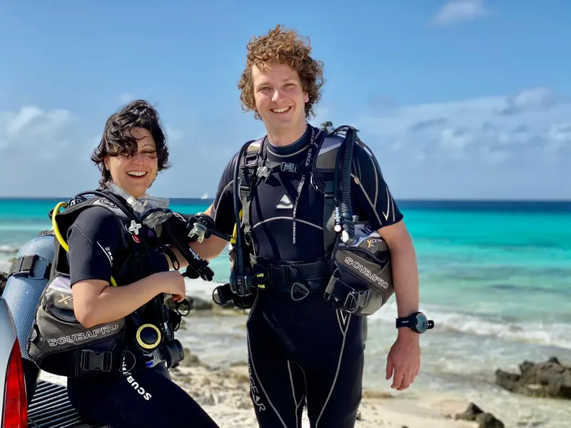 Deux plongeurs souriants en combinaison sur une plage tropicale
