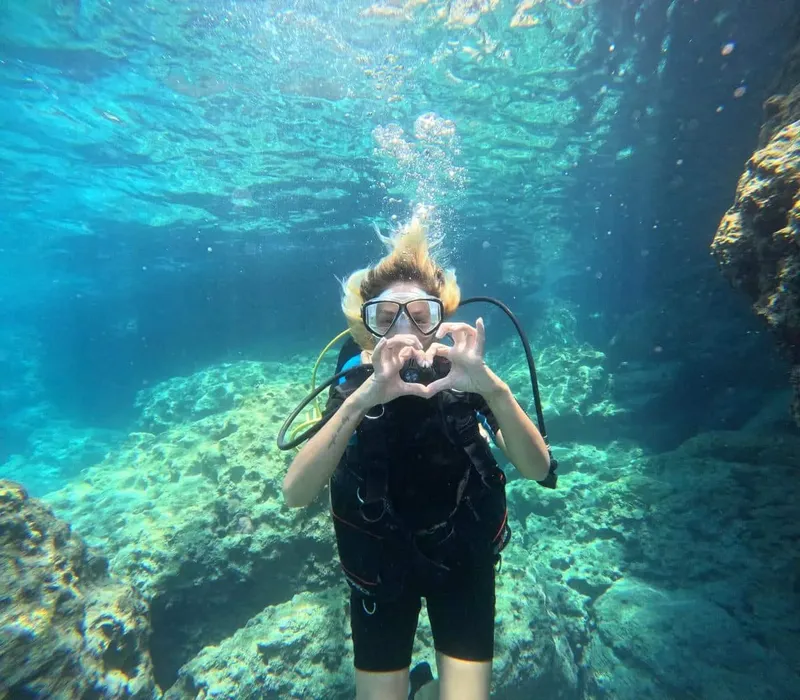 Plongeuse souriante forme un cœur avec ses mains sous l'eau