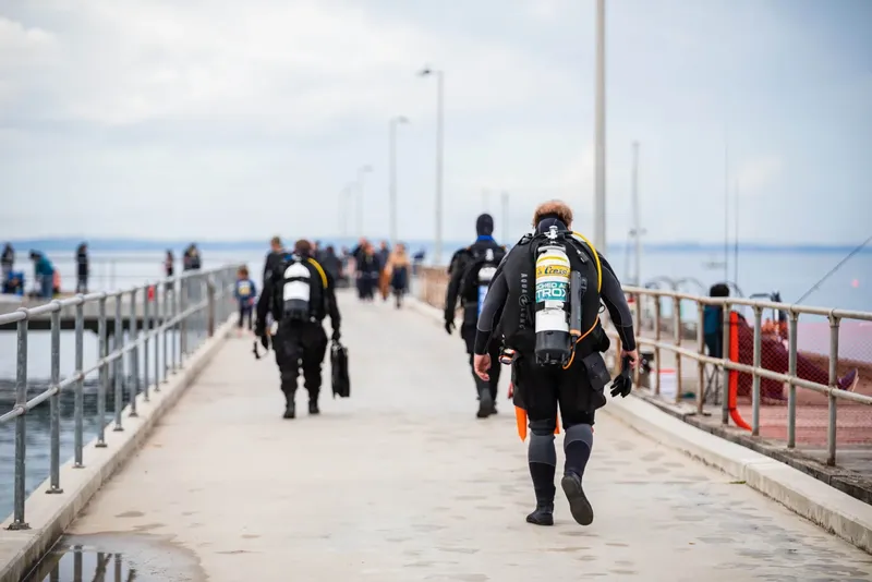 Plongeurs en combinaison marchant sur un ponton vers la mer