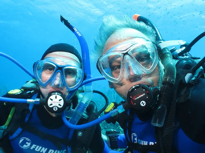 Deux plongeurs souriants avec leur équipement, dans une eau bleue claire