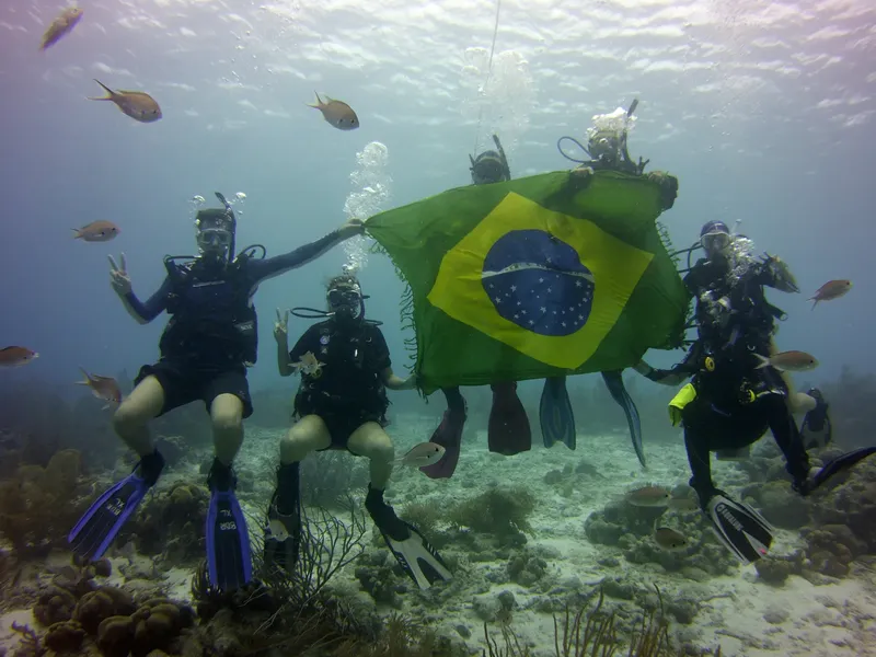 Quatre plongeurs tiennent un drapeau brésilien sous l'eau avec des poissons