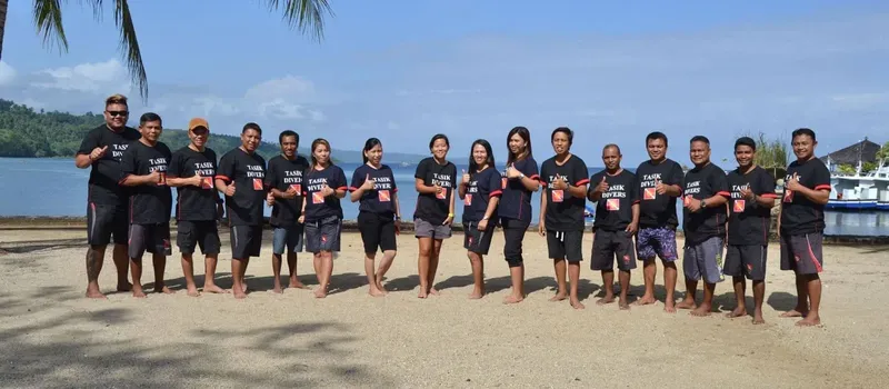 Groupe de personnes souriantes sur une plage ensoleillée avec bateaux en arrière-plan