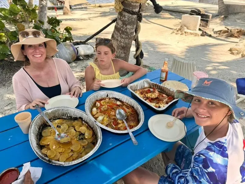 Trois personnes souriantes déjeunent en plein air sur une table bleue