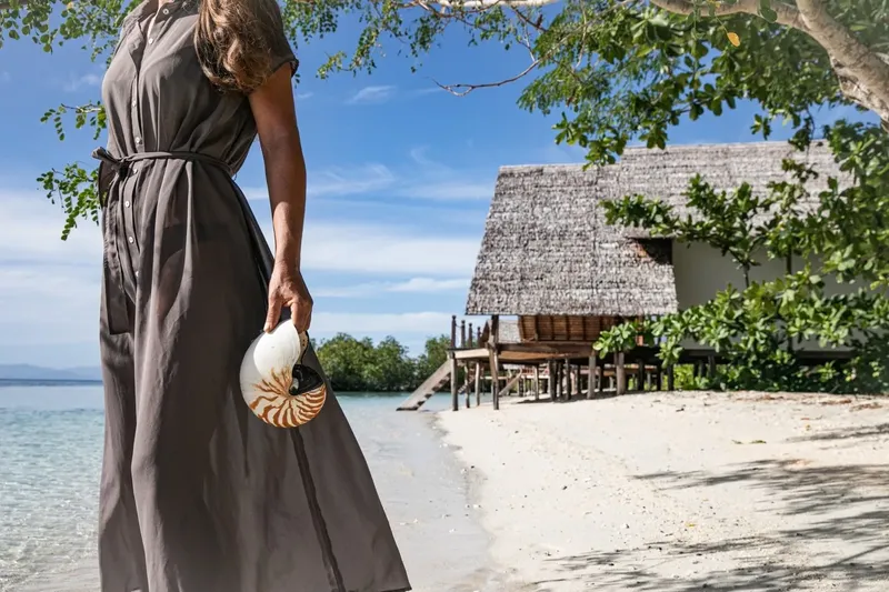 Femme sur plage tenant un coquillage nautile devant une maison