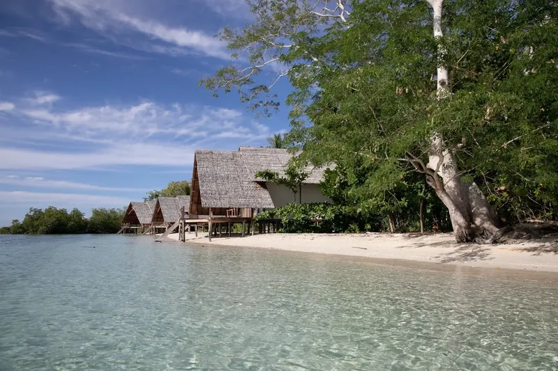 Plage de sable blanc avec bungalows sur pilotis et végétation tropicale