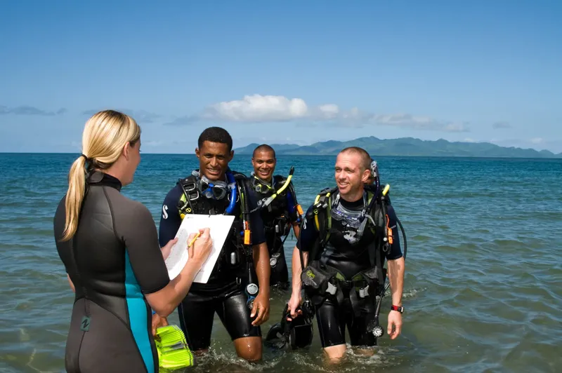 Plongeurs équipés discutent avec une monitrice sur une plage ensoleillée