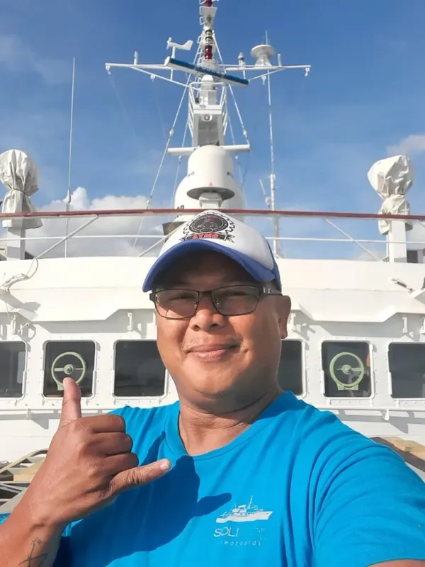 Homme souriant sur un bateau de plongée, pouce levé, ciel bleu