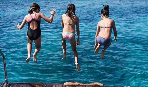 Trois jeunes femmes sautent dans une mer bleue depuis un ponton