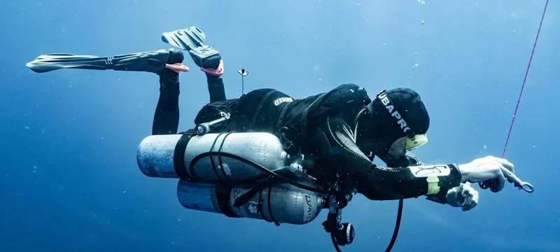 Plongeur en combinaison noire équipé nageant dans une eau bleue claire