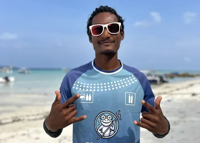 Homme souriant sur une plage, pointant un motif sur son t-shirt