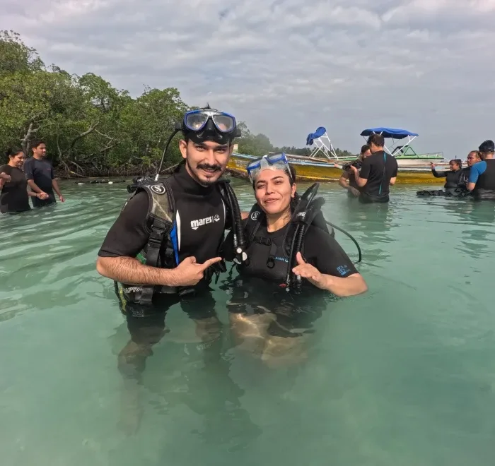 Deux plongeurs souriants dans l'eau turquoise avec équipement complet