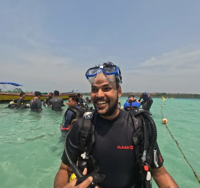 Plongeur souriant avec son équipement dans une eau turquoise peu profonde